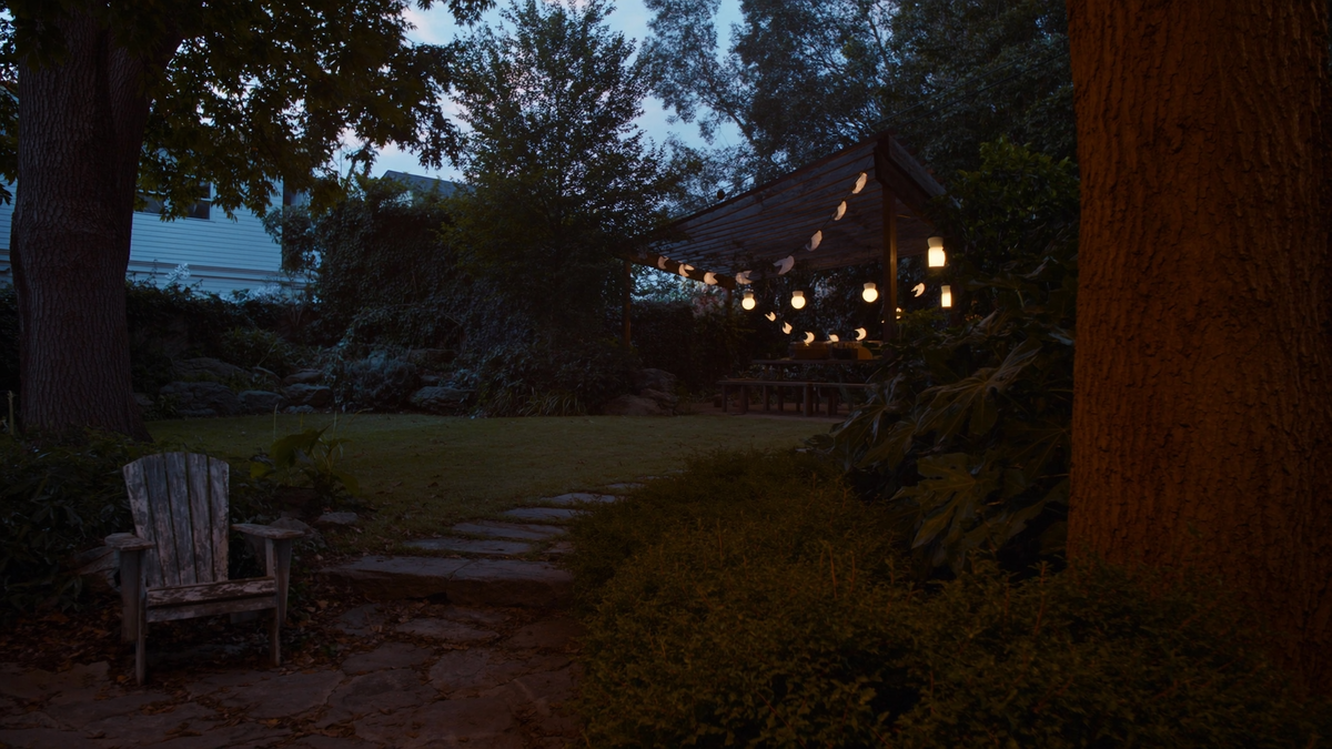 Warm outdoor pendant lights glowing over a pergola and garden path at dusk