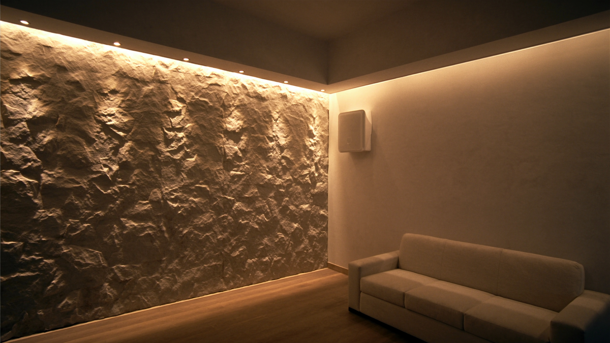 Modern living room with a textured stone accent wall grazed by warm ceiling spotlights and a smooth wall softly washed with light